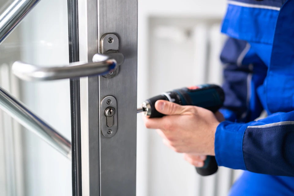 Technicien en combinaison bleue effectuant une intervention de serrurerie sur une porte d'entrée moderne