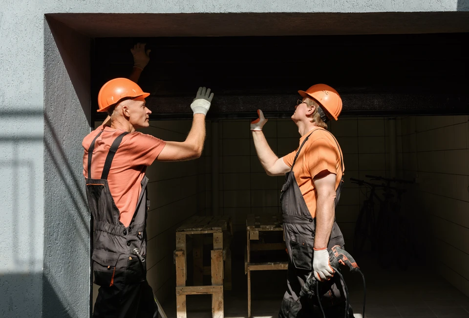 Un technicien en salopette rouge travaille sur une porte vitrée d'un bâtiment commercial moderne